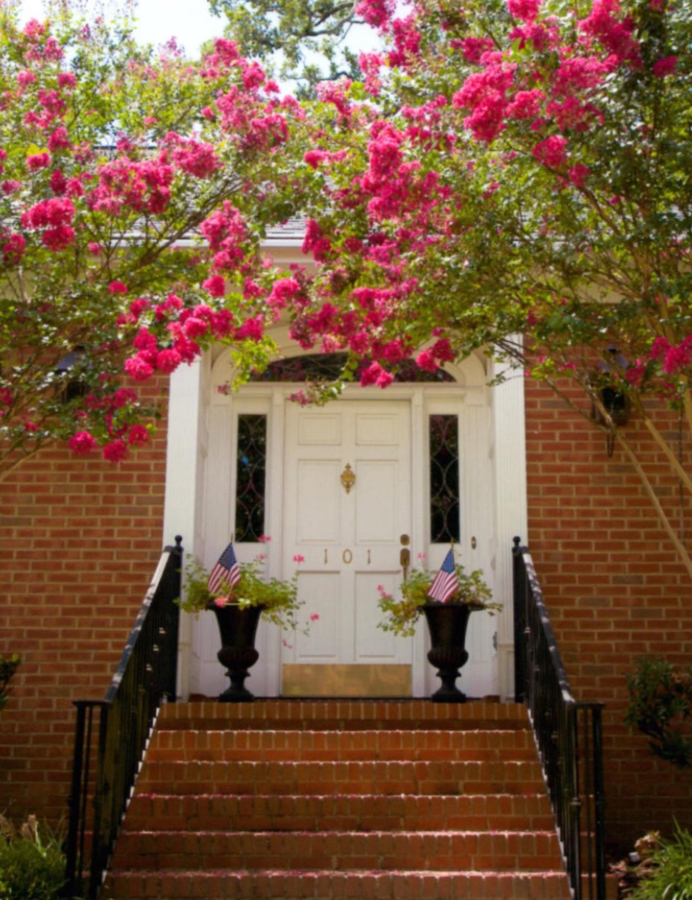White door with pink flowers and American flags on a brick wall