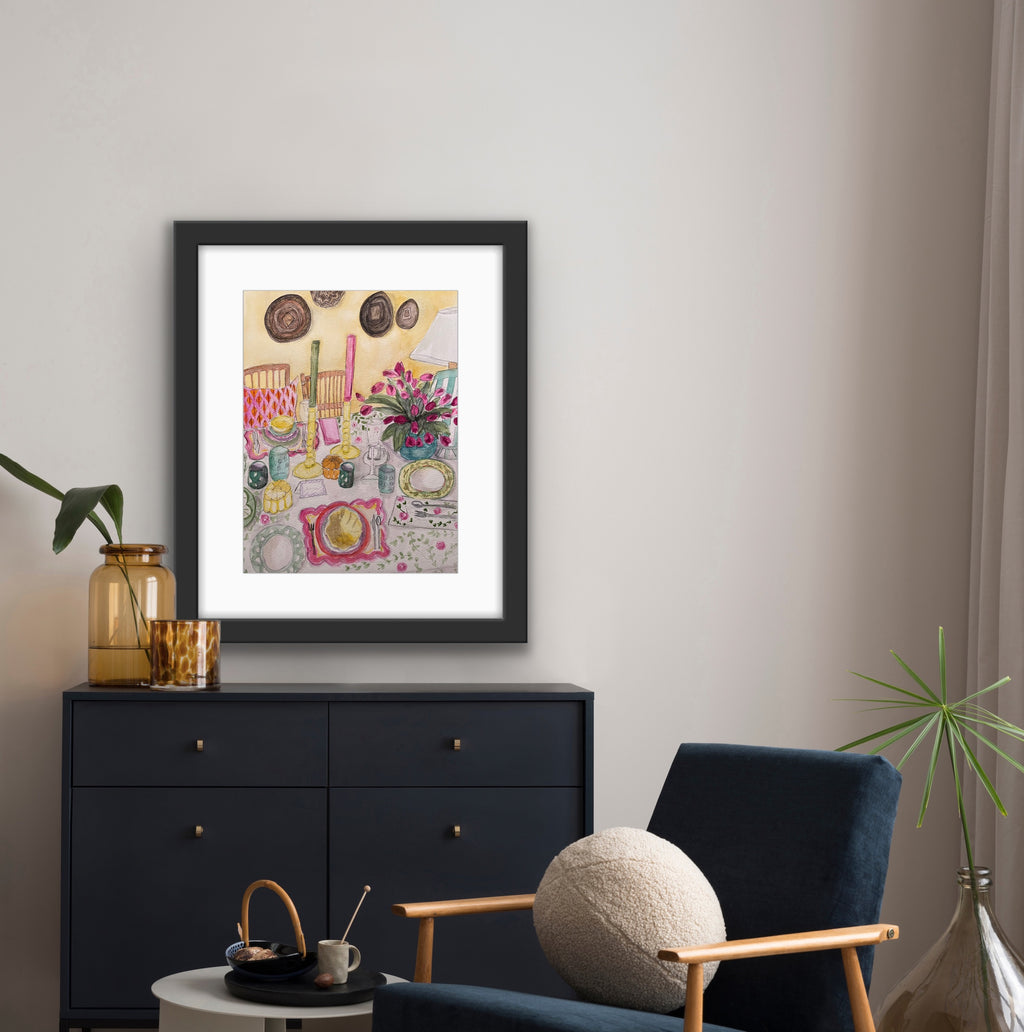 Framed artwork on a wall above a black dresser with a blue chair and decorative items.