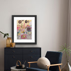 Framed artwork on a wall above a black dresser with a blue chair and decorative items.
