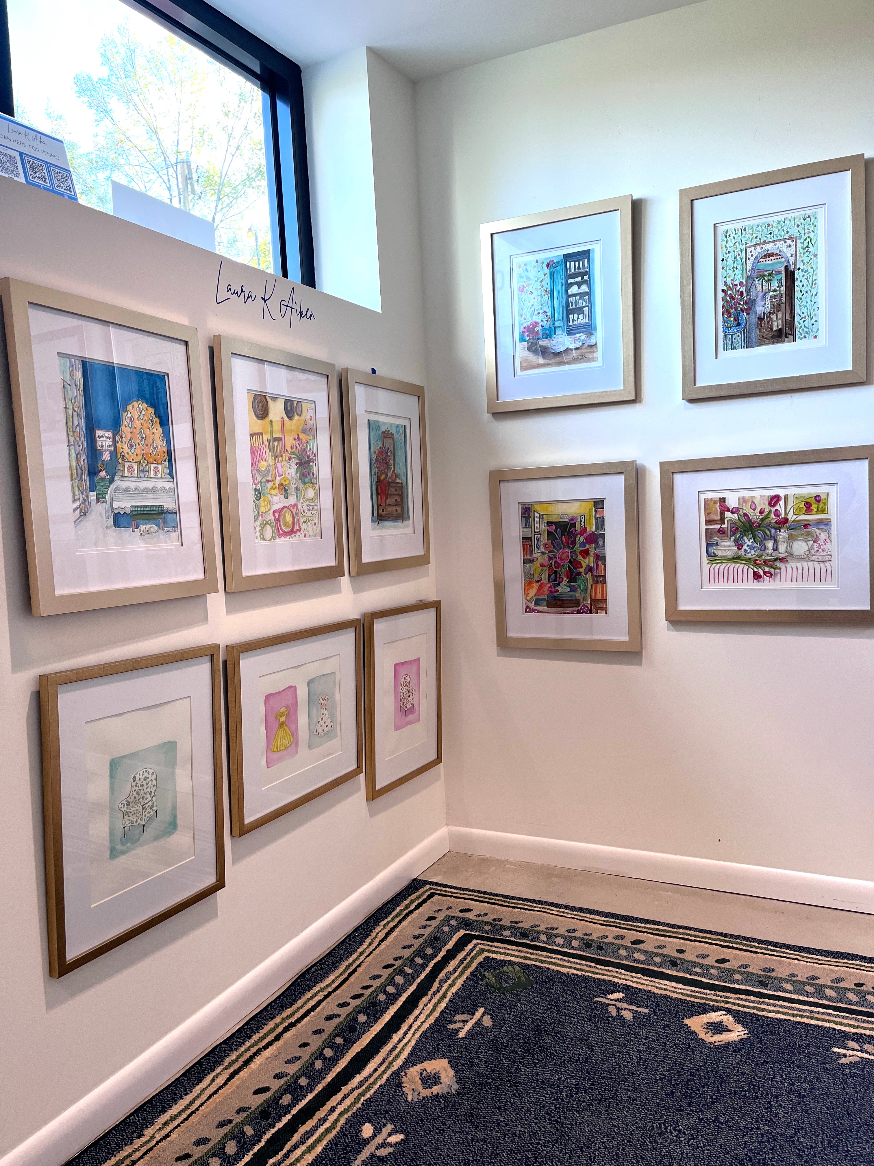 Artistic wall display with framed artworks in a room with a window and rug.